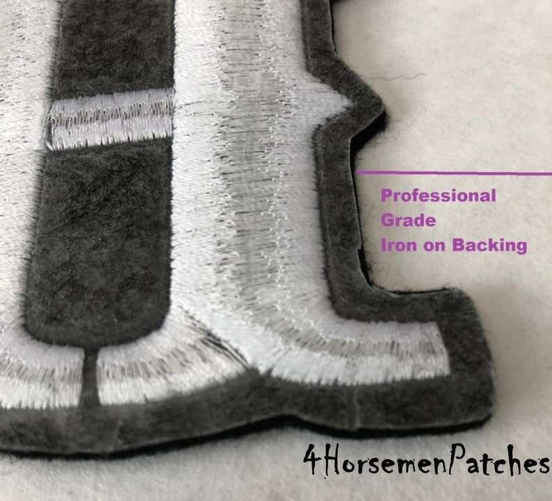 Puede incluir: Primer plano de un parche bordado en gris y blanco con la letra "F" y un respaldo termoadhesivo de calidad profesional. El parche est&aacute; hecho con materiales de alta calidad y es perfecto para agregar un toque personalizado a la ropa, bolsos u otros art&iacute;culos.