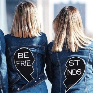 May include: Two denim jackets with black heart-shaped patches on the back. The patches are split in half and say "BE FRIE" and "ST NDS" in white text.