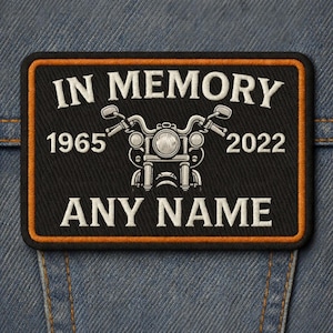 May include: Black rectangular patch with an orange border, featuring a motorcycle graphic and the text "IN MEMORY" above "ANY NAME". Dates "1965" and "2022" flank the motorcycle design. The patch is set against a denim background.
