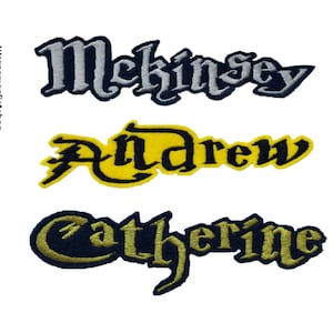 May include: Three embroidered iron-on patches with names in a gothic font. The top patch is silver with the name "McKinsey". The middle patch is yellow with the name "Andrew" in black. The bottom patch is navy blue with the name "Catherine" in gold.