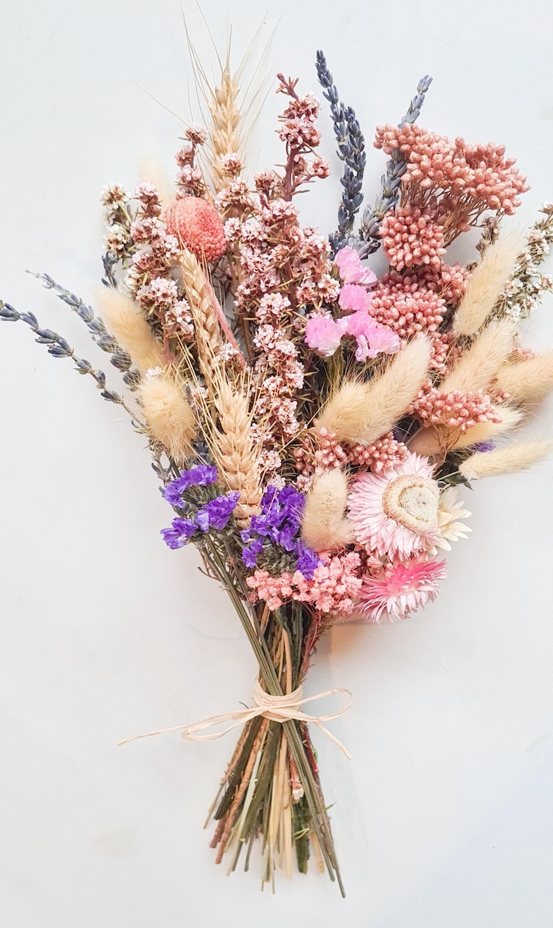 Dried flower bridal bouquet in soft pink, lilac and neutral tones tied with raffia, on a white background.