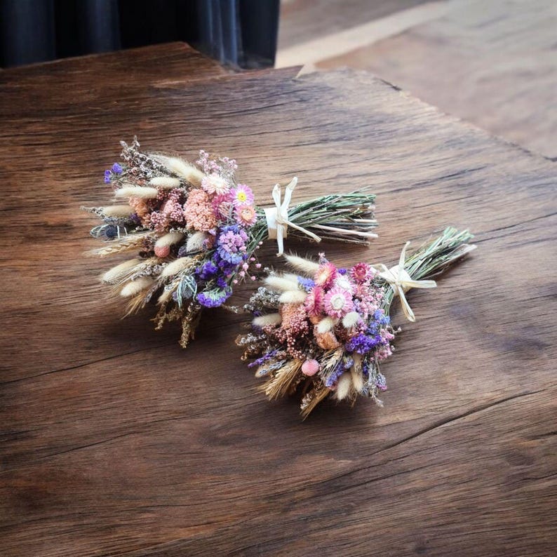 Dried flower bouquet in soft pink, lilac and neutral tones tied with raffia, styled on a dark wooden surface.
