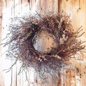 May include: A dried floral wreath made of brown twigs and dried flowers. The wreath is hanging on a wooden wall.