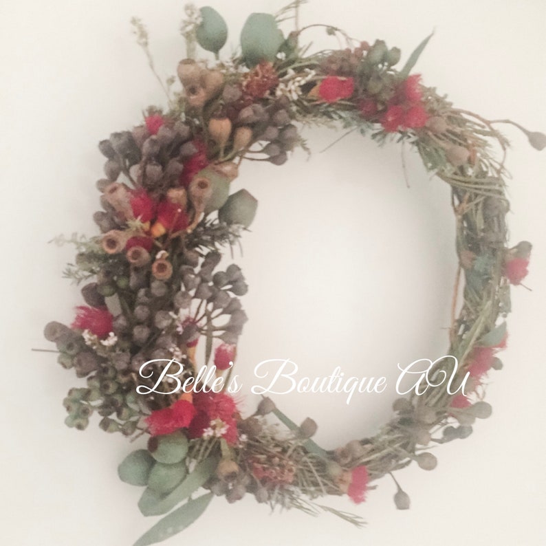 A  floral wreath featuring red, brown, and green accents. The wreath is crafted with eucalyptus, gumnuts and other dried and fresh flowers. Created by Belle's Boutique AU