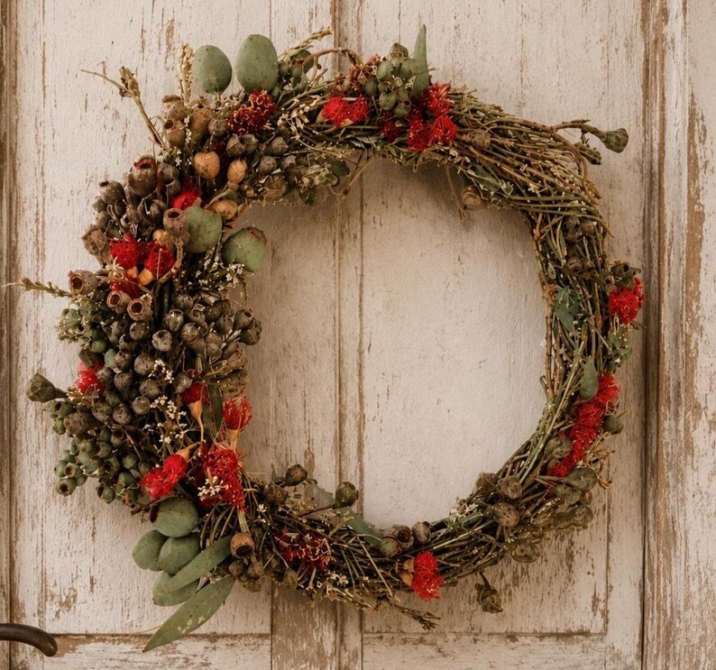 Handmade Australian native dried flower wreath featuring eucalyptus gum nuts, bottlebrush, preserved foliage and rustic twigs, displayed on a weathered white timber door with vintage hardware. An everlasting wreath perfect for front door décor, farmhouse styling, Christmas or Australian home décor
