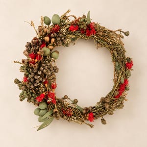 Australian native dried and fresh flower wreath featuring red eucalyptus flowers, gumnuts, seed pods and eucalyptus foliage on a natural twig base against a warm neutral background.