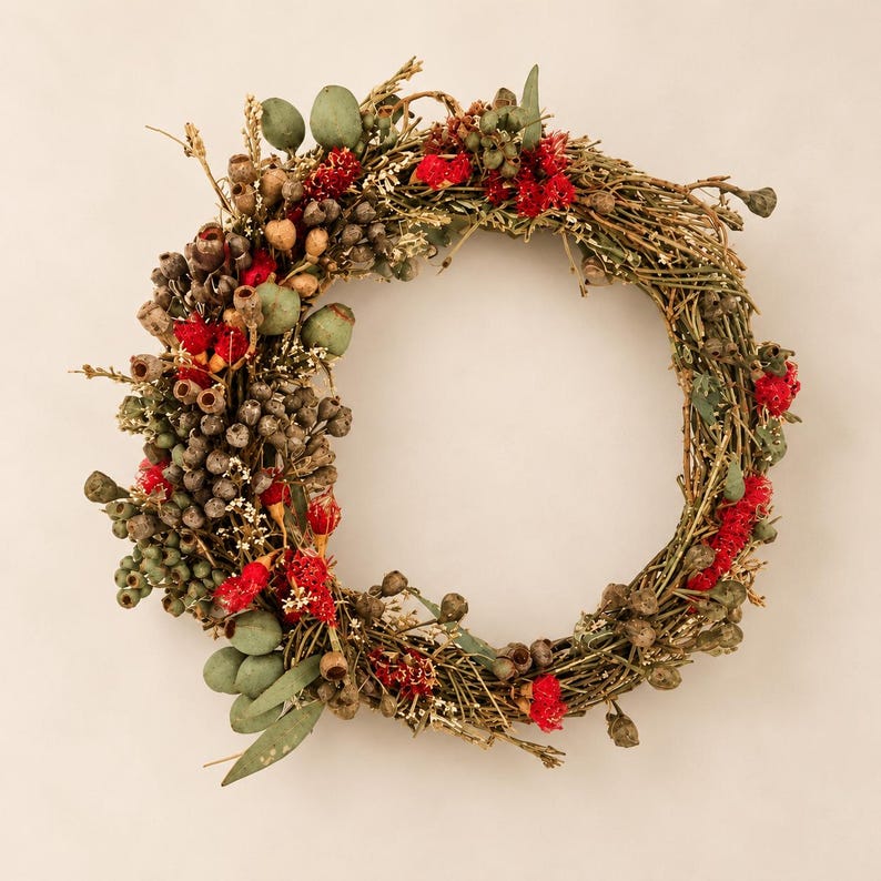 Australian native dried and fresh flower wreath featuring red eucalyptus flowers, gumnuts, seed pods and eucalyptus foliage on a natural twig base against a warm neutral background.