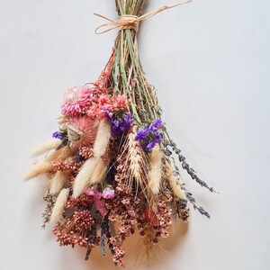 Dried flower bridal bouquet in soft pink, lilac and neutral tones tied with raffia, on a white background.