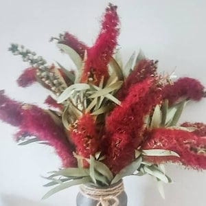 Peut inclure: Un bouquet de fleurs séchées rouges et de feuilles vertes dans un vase brun avec un nœud en ficelle.