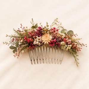 Könnte beinhalten: Ein Haarkamm mit einem Arrangement aus getrockneten Blumen und Blättern in Rosa-, Creme- und Grüntönen. Das dekorative Blumenarrangement ist an einem silberfarbenen Metallkamm mit mehreren Zinken befestigt, ein botanisches Haaraccessoire.