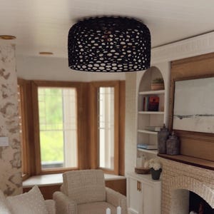 May include: Miniature living room scene with white textured sofas, a wooden coffee table, and a fireplace. A gold side table with a lamp and a black patterned ceiling light complete the cozy interior design.