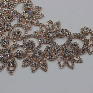 May include: A delicate rose gold rhinestone trim with a floral design. The trim is made of small, clear rhinestones set in a rose gold metal base.