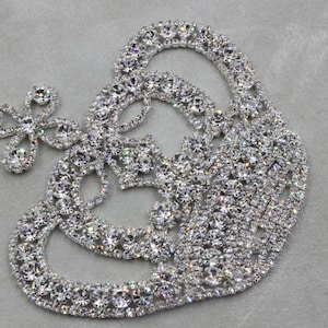 May include: A silver rhinestone applique in the shape of a crown with a smaller flower design on the side.