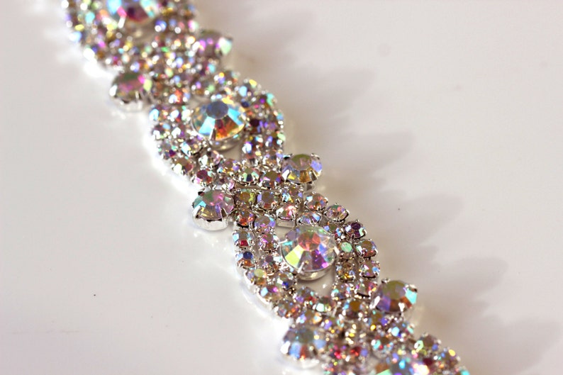 May include: A silver-toned, iridescent rhinestone trim with a repeating pattern of small and large rhinestones.