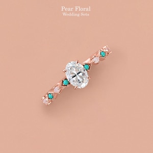 May include: A rose gold ring featuring a central oval-cut clear stone, accented with alternating small turquoise and white round stones along the band. The text "Pear Floral Wedding Sets" is printed above the ring on a solid light peach background.