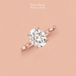 May include: A rose gold ring featuring a large oval-cut center stone held by four prongs. The band is accented with alternating small round clear stones and small round white stones, with the text Pear Floral Wedding Bands visible above.