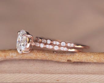 May include: A rose gold engagement ring set with a large oval-shaped center stone and a delicate band of smaller stones.