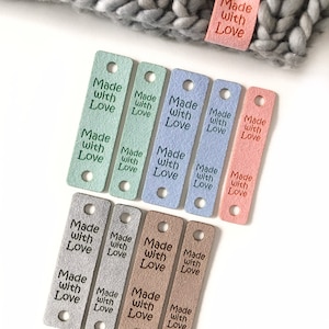 May include: Assortment of colourful leather tags with the text "Made with Love" in black lettering. The tags are in various colours, including pink, blue, green, brown, and grey.