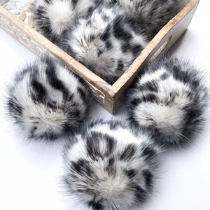 May include: Five black and white faux fur pom poms in a wooden tray. The pom poms are fluffy and have a zebra-like pattern.