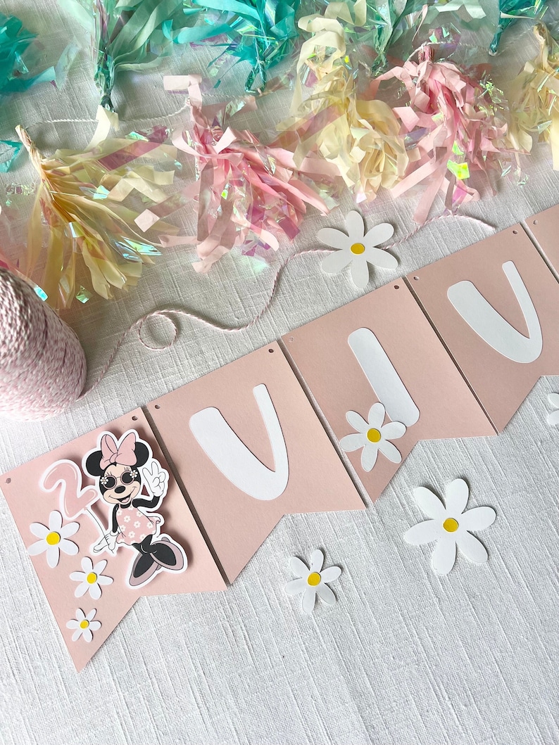 Puede incluir: Bandera rosa y blanca con la palabra "Viva" en letras blancas y una imagen de dibujos animados de Minnie Mouse con gafas de sol y un vestido rosa. La bandera est&aacute; decorada con margaritas blancas.