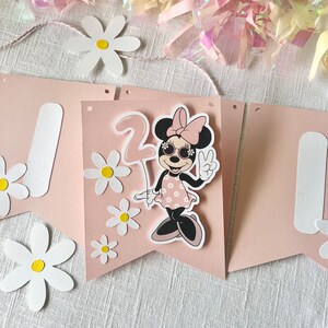 Puede incluir: Una pancarta rosa y blanca con una imagen de dibujos animados de un rat&oacute;n con gafas de sol y sosteniendo un globo. La pancarta tiene el n&uacute;mero "2" y est&aacute; decorada con margaritas blancas.