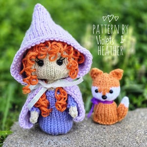 May include: Hand-knitted doll with orange curly hair, wearing a purple dress and hat, and a matching cape. A small orange fox with a purple ribbon sits beside the doll. The text "PATTERN BY VIOLETS & HEATHER" is visible.