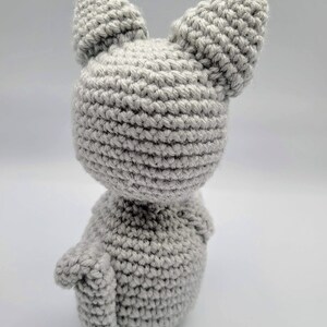 May include: A gray crocheted cat toy with large ears. The cat is sitting on a white surface.