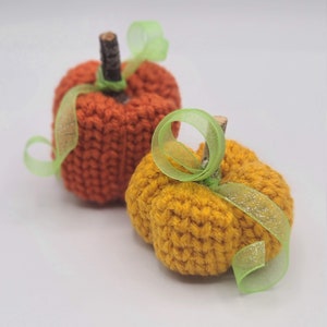 May include: Two knitted pumpkins, one orange and one yellow, with green ribbon accents.