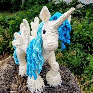 May include: A white crocheted unicorn with blue and light blue yarn mane and tail. The unicorn has a white horn and wings.