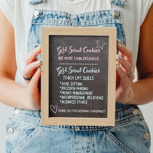 Puede incluir: Un letrero de pizarra enmarcado con el texto "Girl Scout Cookies are more than delicious. Girl Scout Cookies teach life skills: *Goal Setting *Decision Making *Money Management *Interpersonal Relations *Business Ethics. Thank you for inspiring confidence!"