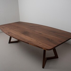 May include: A large, rectangular, wooden dining table with a dark brown walnut finish. The table has a slightly curved edge and sits on a simple, modern, triangular base.