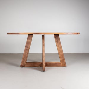 May include: A wooden oval table with a unique triangular base. The table is made of dark wood and has a natural finish.