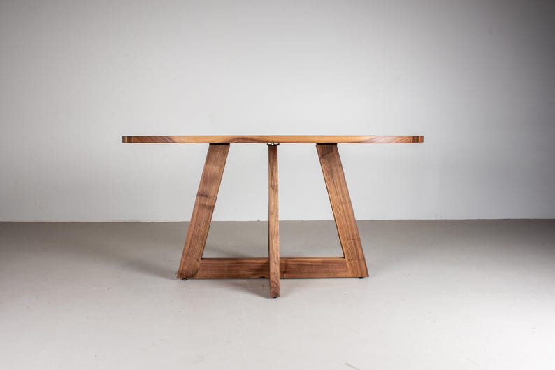 May include: A wooden oval table with a unique triangular base. The table is made of dark wood and has a natural finish.