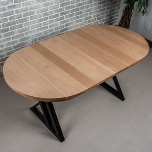 May include: A light wood oval table with a black metal triangular base. The table top is made of wood planks.