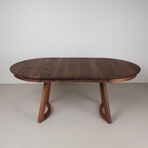 May include: A dark brown oval wooden table with a simple design. The table has a smooth, polished finish and is supported by four legs.
