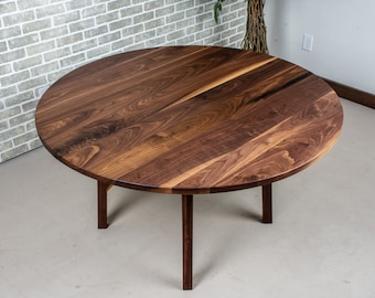 May include: A round, dark brown wooden table with a smooth, polished surface. The table has four legs that are slightly angled inwards.