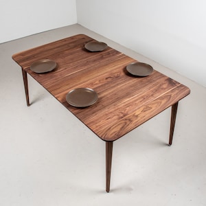 May include: A rectangular wooden dining table with four brown ceramic plates on the surface. The table has four slender legs.