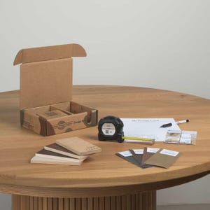 May include: A design kit with a cardboard box, tape measure, samples, and a design card on a wooden table. The tape measure shows 35 inches. The kit includes color swatches and a pen.