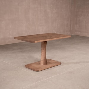 May include: A solid wood table with a rectangular top, supported by a curved pedestal and a rectangular base. The table is a warm brown color and appears to be made of a single piece of wood. The table is approximately 30 inches long.
