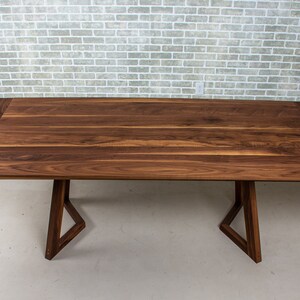 May include: A dark brown wooden dining table with two leaves that extend the table's length. The table has a modern, triangular base.