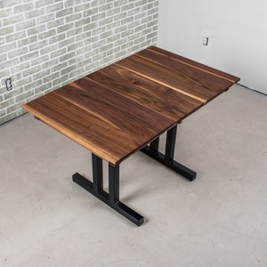 May include: A rectangular wooden table with a black metal base. The table top is made of walnut wood and has a natural finish. The table is shown from an overhead perspective.