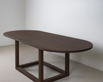 May include: A dark brown, oval-shaped wooden table. The table has a rectangular base with four legs and a smooth, solid surface. The table is made of wood and has a natural finish.
