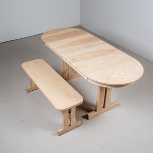May include: A light wood oval table with a matching bench. The table has a simple design with straight legs and a rounded top. The bench is also simple with straight legs and a rectangular top.