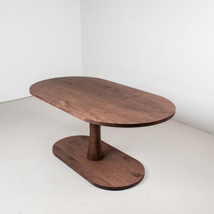 May include: A dark brown oval wooden table with a unique pedestal base. The table top is smooth and the base is slightly curved.