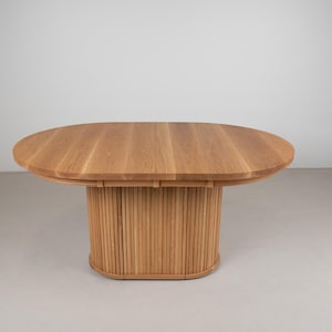 May include: A light wood oval dining table with a slatted base. The table top is made of solid wood and has a natural finish.