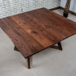 May include: A square wooden table with a dark brown walnut finish. The table has a simple, modern design with a triangular base.