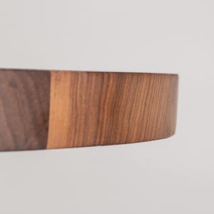 May include: A close-up of a round wooden cutting board made of walnut wood. The board has a natural wood finish and is perfect for serving cheese, charcuterie, or other appetizers.