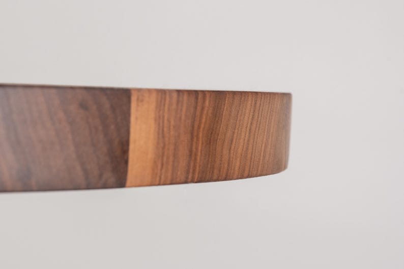 May include: A close-up of a round wooden cutting board made of walnut wood. The board has a natural wood finish and is perfect for serving cheese, charcuterie, or other appetizers.