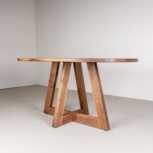 May include: A wooden oval table with a natural wood finish and a unique A-frame base.