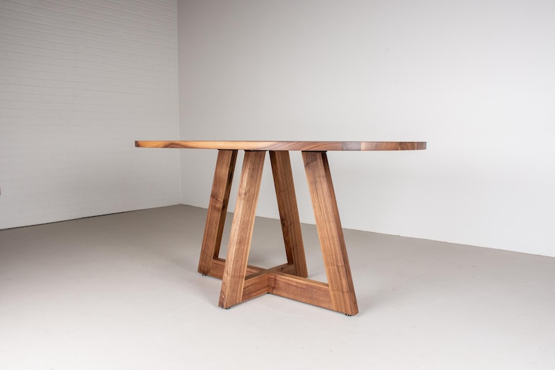 May include: A wooden oval table with a natural wood finish and a unique A-frame base.